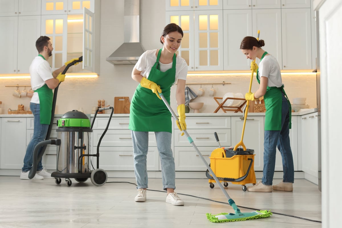 Professional cleaning team in uniforms working in a kitchen with equipment
