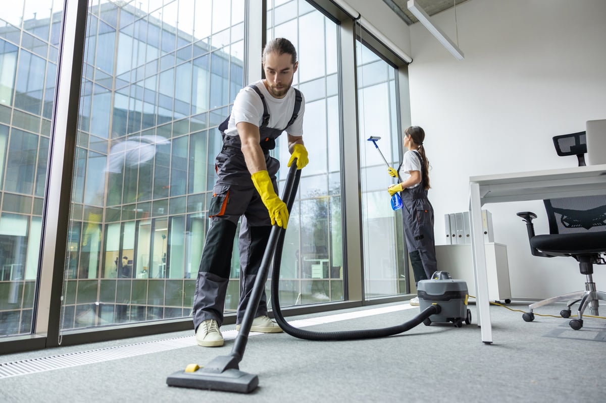 Young man in uniform vacuum cleaning the floor in a conference room