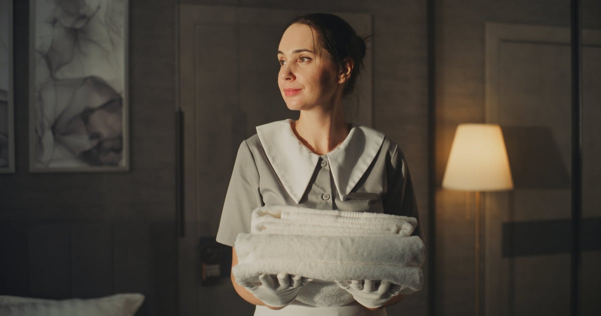 Hotel maid in classic uniform with white gloves holding clean towels